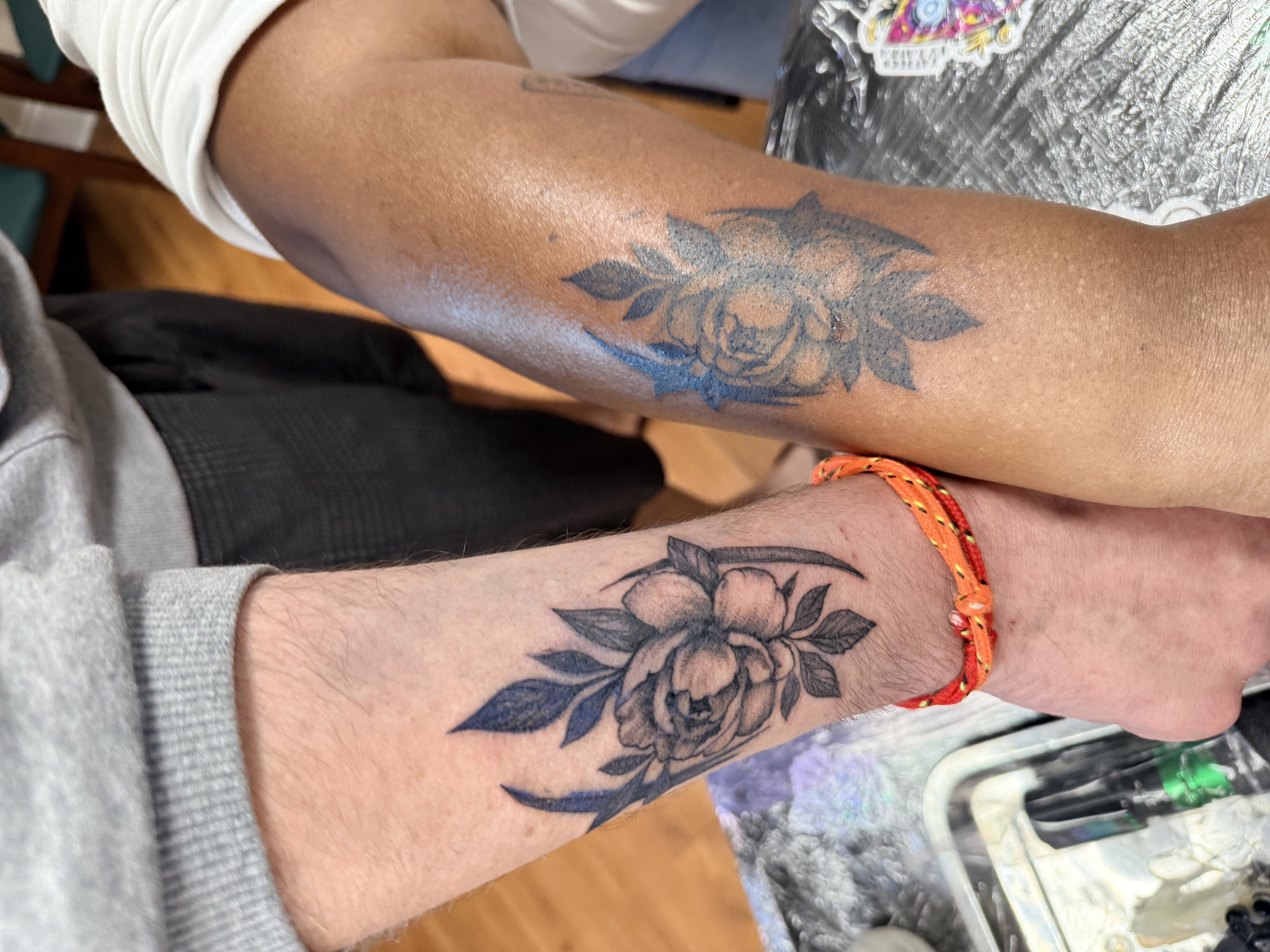 Matching black and grey rose tattoos on two forearms side by side