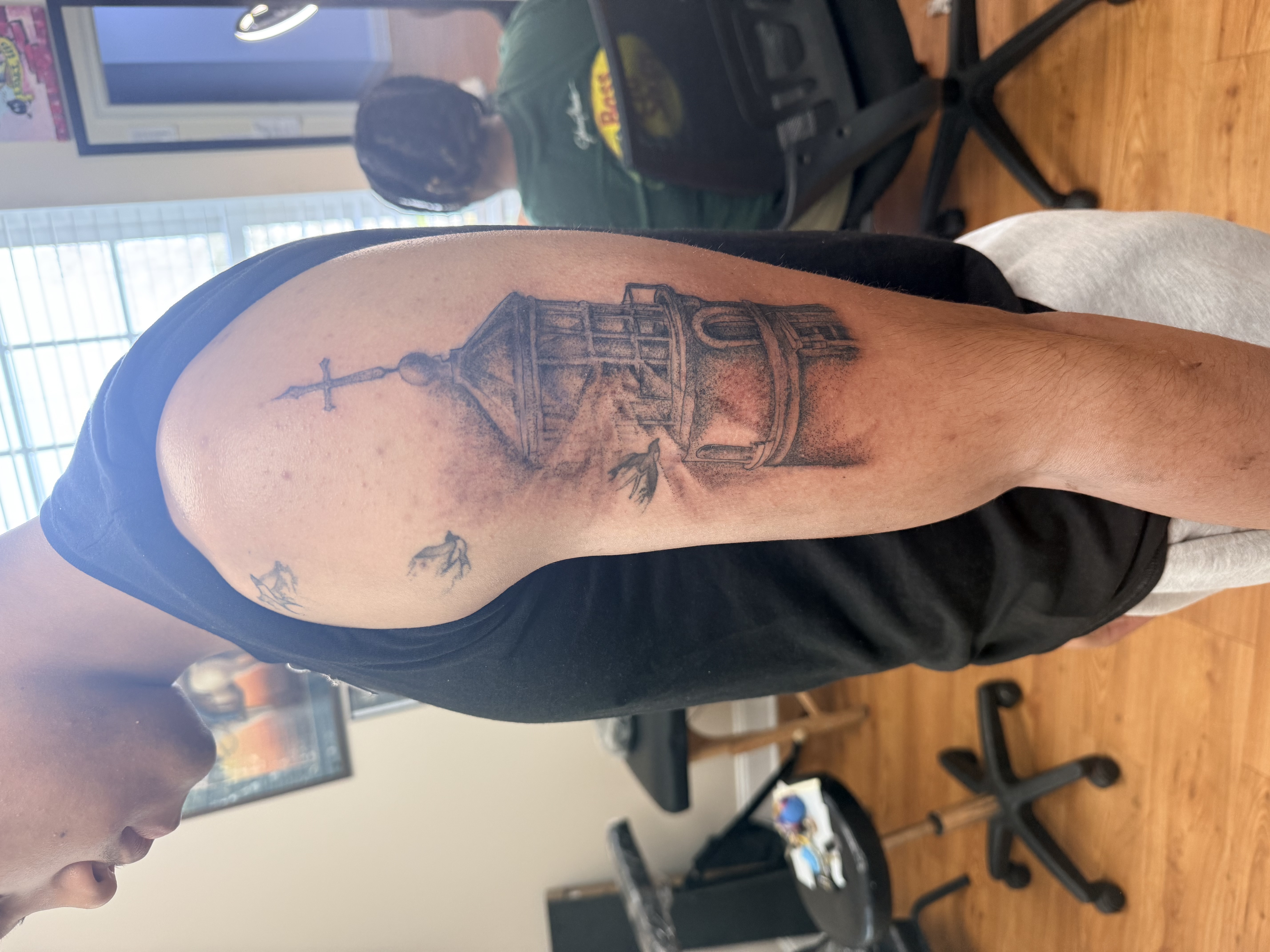 Detailed black and grey lighthouse tattoo on the upper arm — sketch style